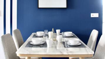 A dining area with a marble table, grey upholstered chairs, and a blue wall with a framed picture.