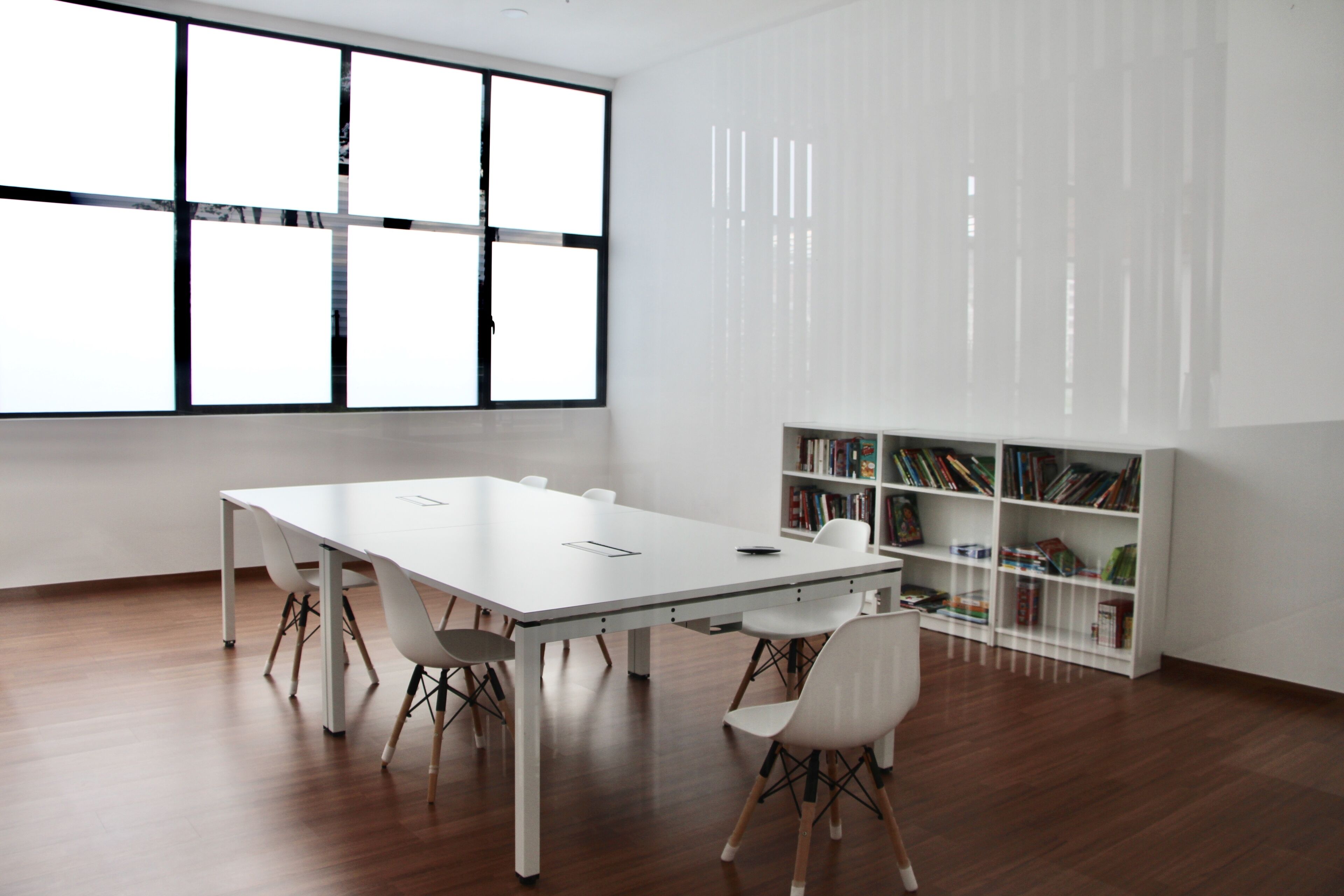 A modern conference room with a white table, white chairs, and a bookshelf filled with books.