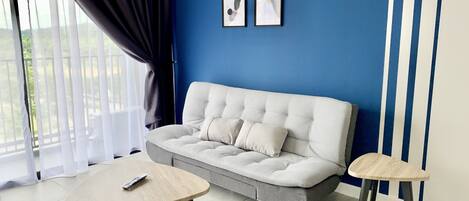 A modern living room with a grey sofa, two small round tables, and a large window with curtains.