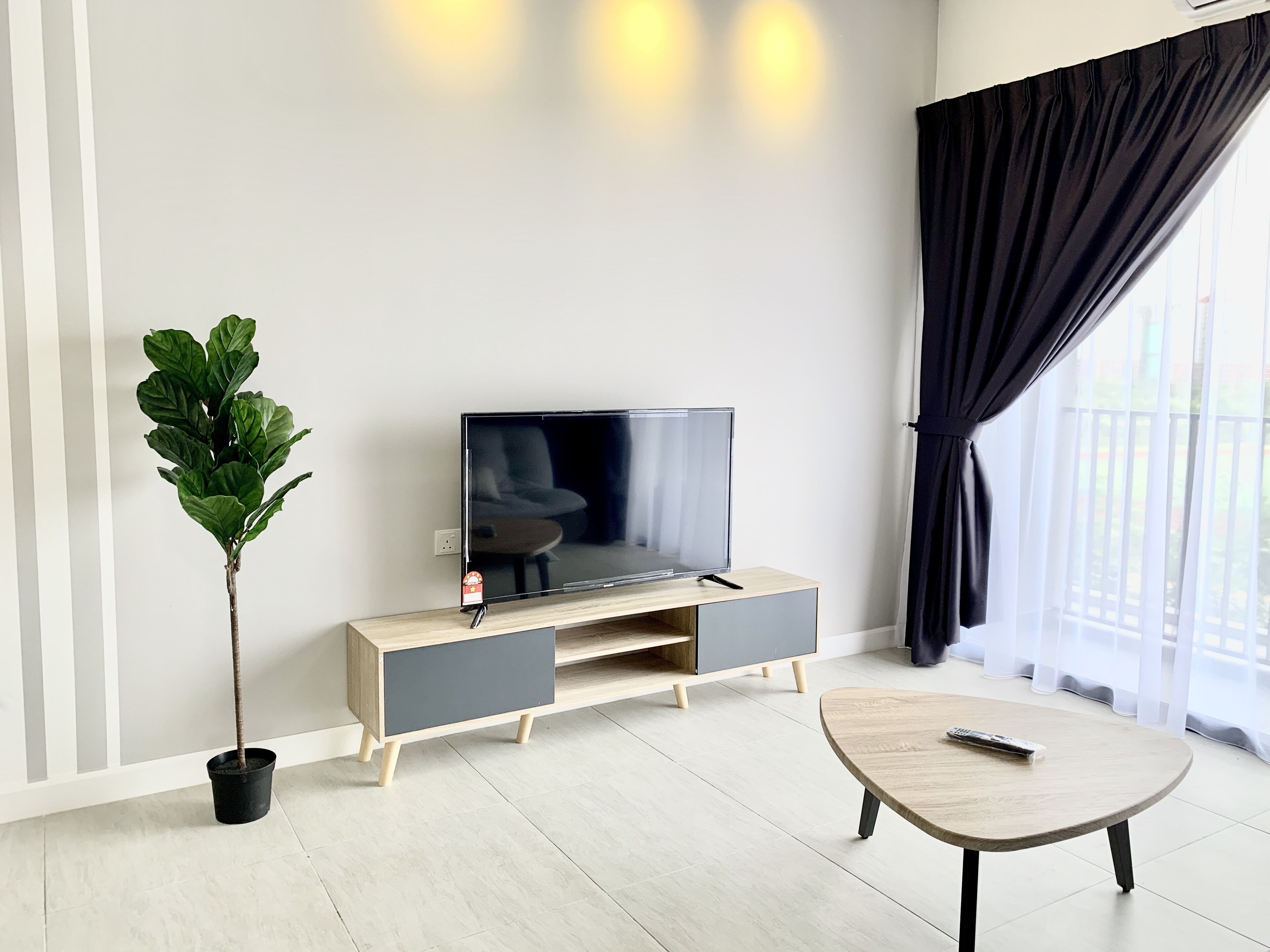 A modern living room with a flat-screen TV on a wooden TV stand, a potted plant, and a round coffee table.