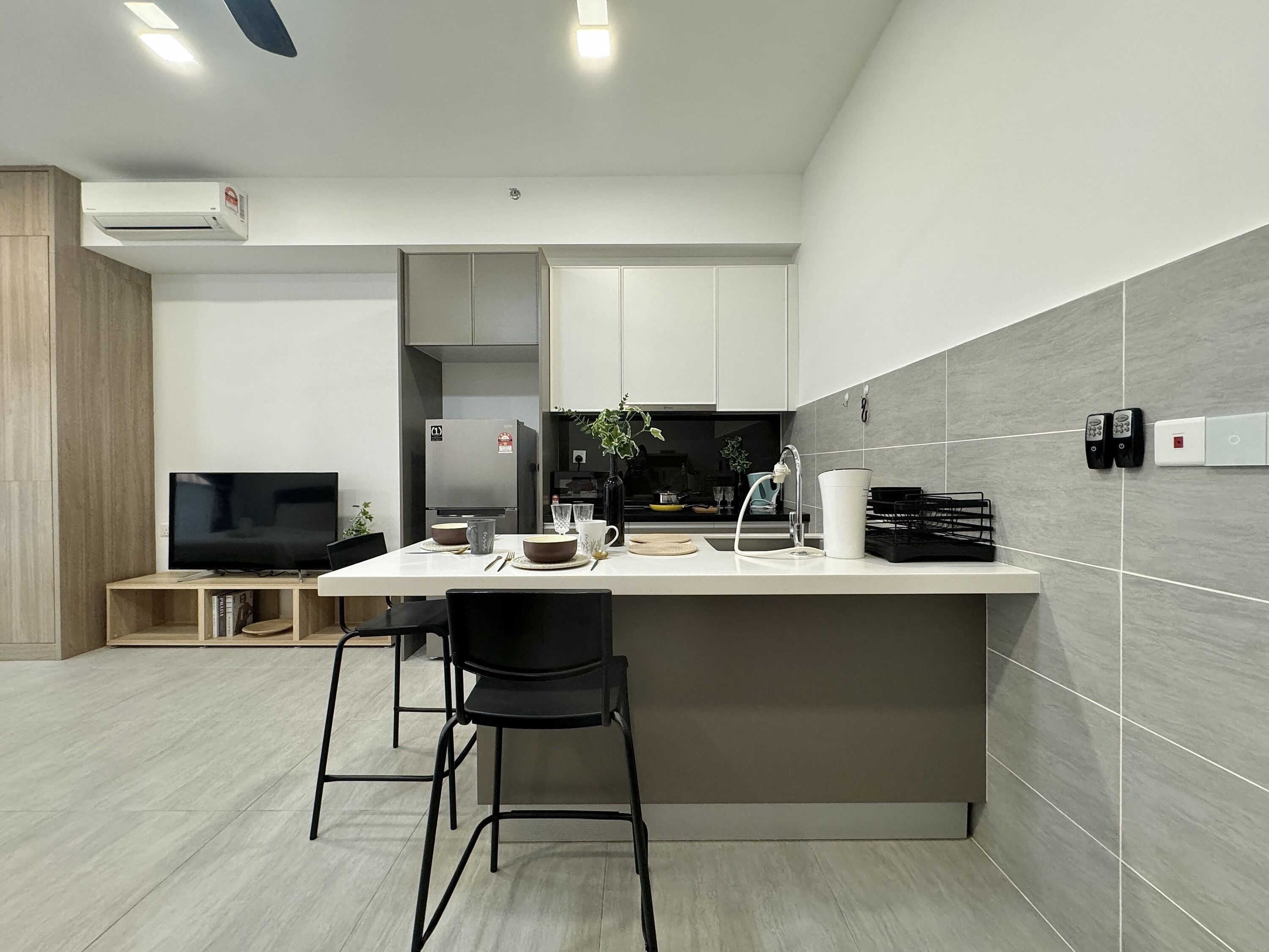 A modern kitchen with a central island, bar stools, a built-in TV, and a dining area.