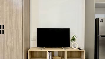 A modern kitchen with a built-in TV on a wooden stand, a refrigerator, and a small plant.