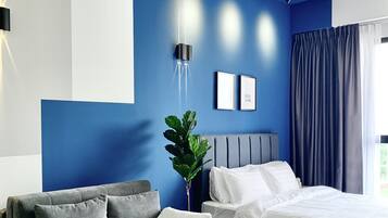 A modern bedroom with a blue accent wall, a grey sofa, a wooden coffee table, and a bed with white bedding.