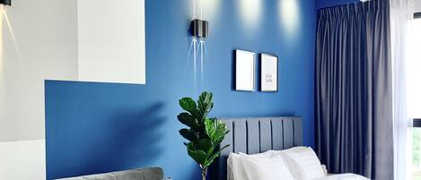 A modern bedroom with a blue accent wall, a grey sofa, a wooden coffee table, and a bed with white bedding.