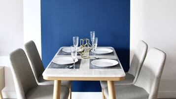 A dining table set with plates, glasses, and cutlery, flanked by two upholstered chairs, against a blue accent wall.