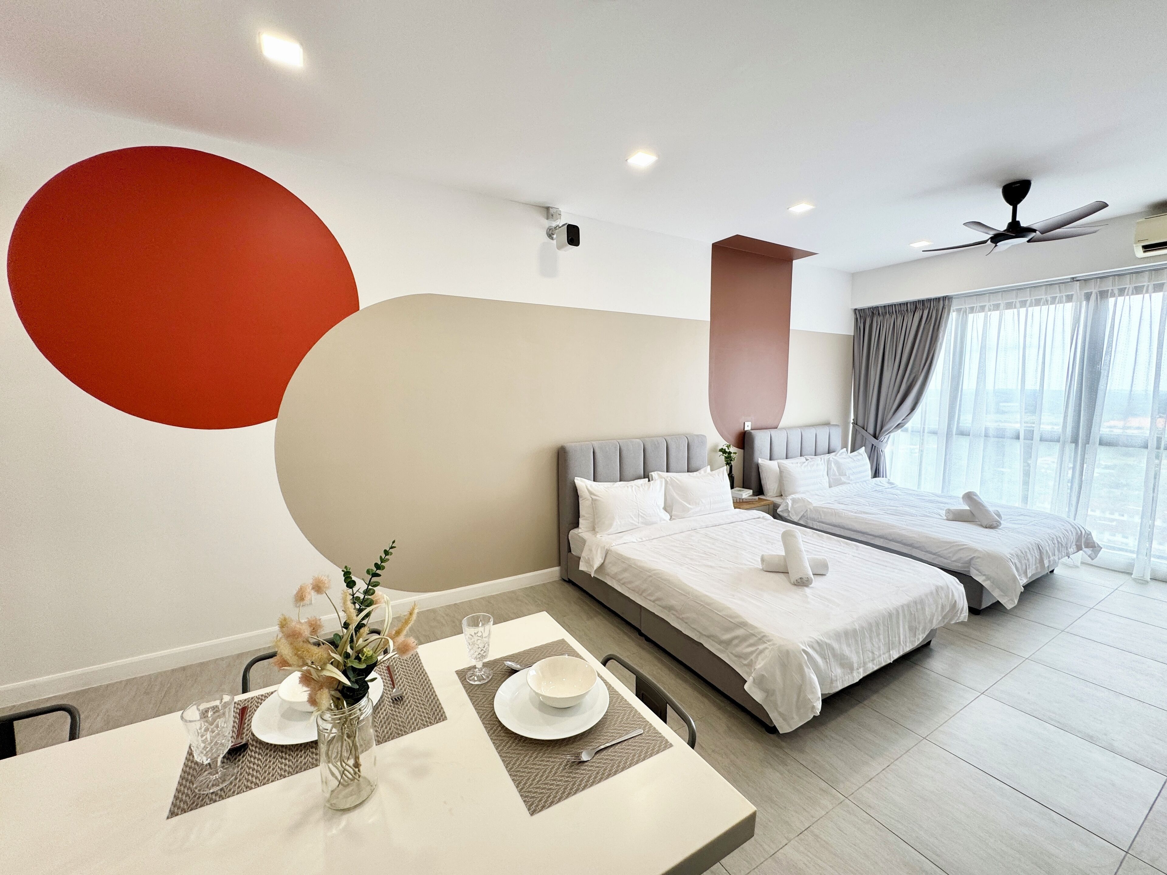 A modern hotel room with two beds, a dining area, and a large window with a view.