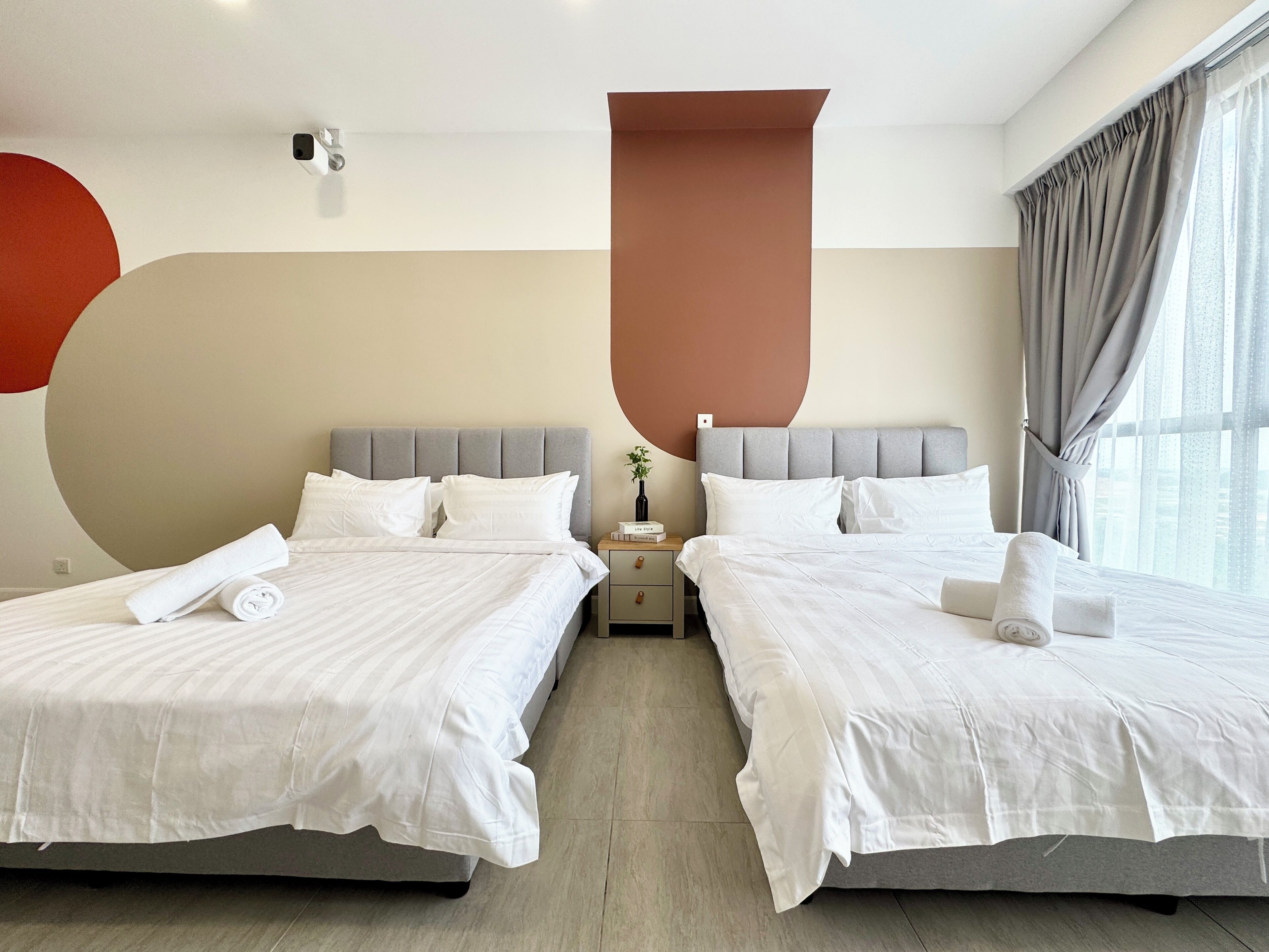 A hotel room with two beds, a nightstand, a vase with a plant, and a large window with curtains.