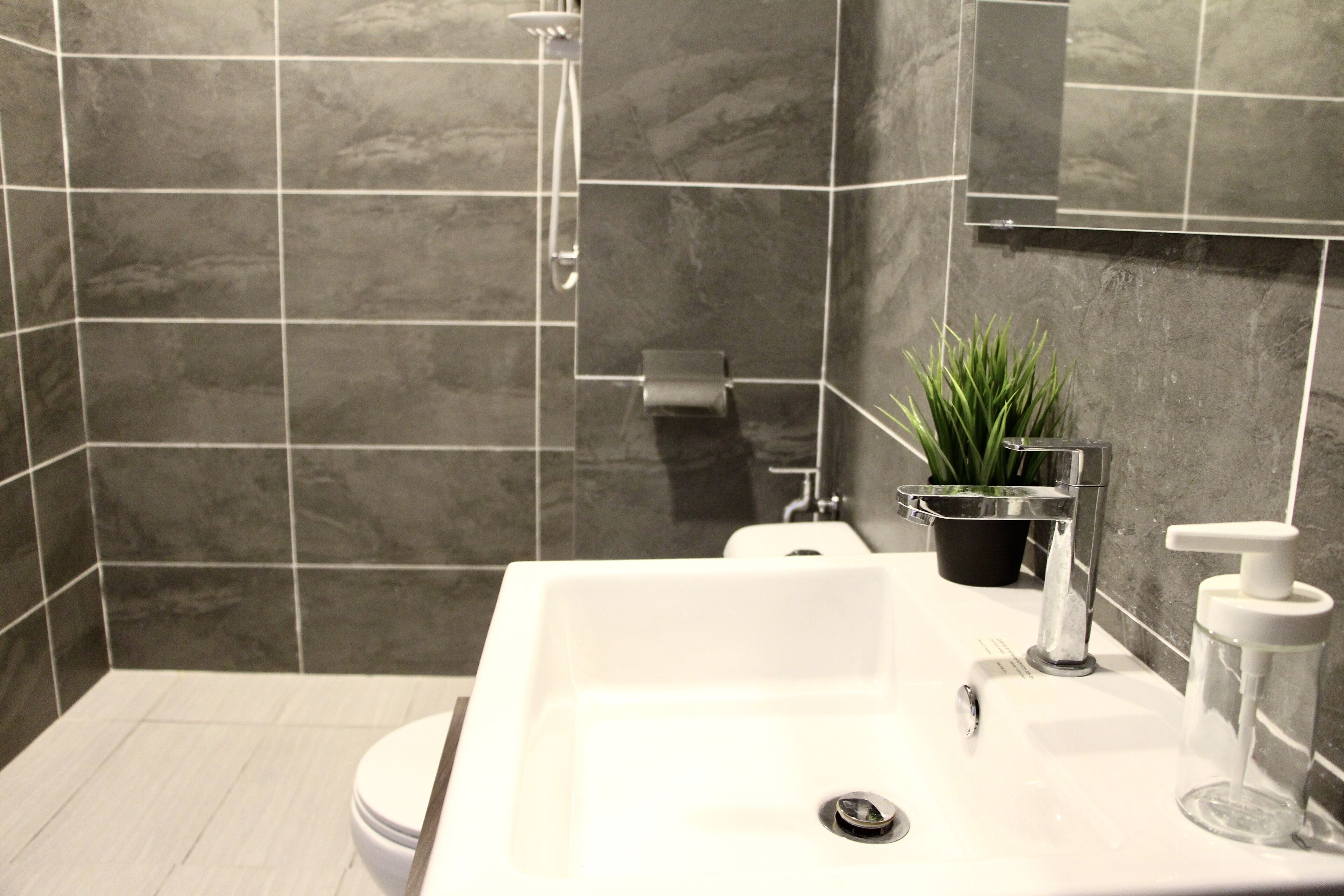 Et moderne badeværelse med vask, håndbruser, en potteplante og toilet.
