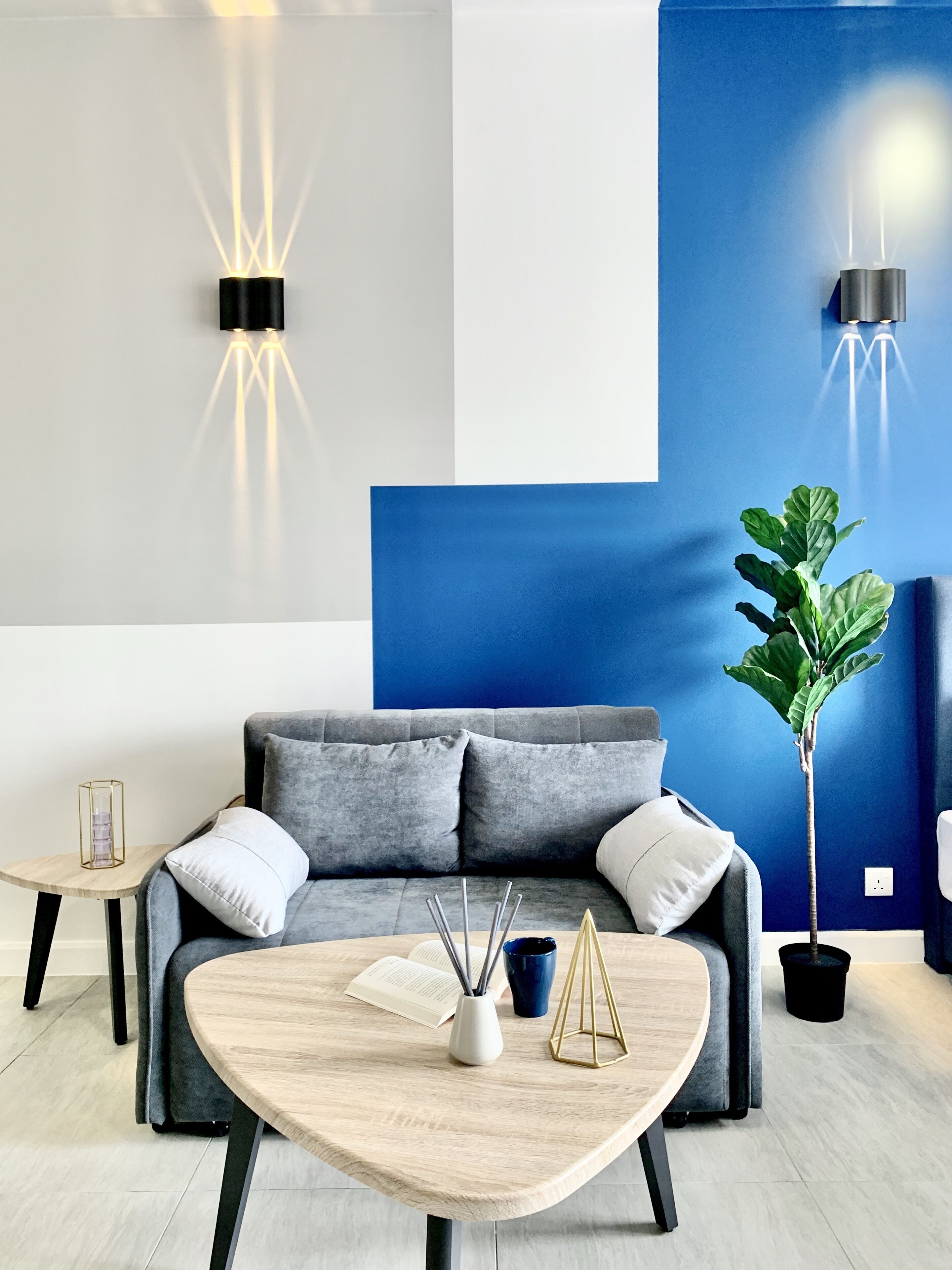 A modern living room with a grey sofa, a wooden coffee table, and a large blue accent wall.