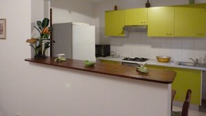 Una cocina con un refrigerador blanco, gabinetes amarillos, una encimera de madera y una planta verde.