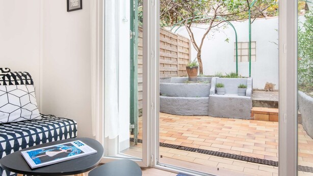 A modern living room with a sofa and a coffee table, a sliding glass door leading to an outdoor patio with a brick floor and potted plants. - MaisonMars Studio 3 Blancarde (Marseille)