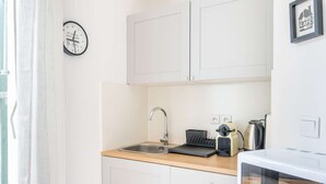 A kitchen with white cabinets, a stainless steel sink, a kettle, a toaster, and a clock on the wall. - MaisonMars Studio 3 Blancarde (Marseille)