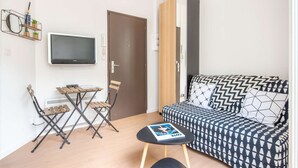 A compact living space with a sofa, a small table, a TV, and a door. - MaisonMars Studio 3 Blancarde (Marseille)