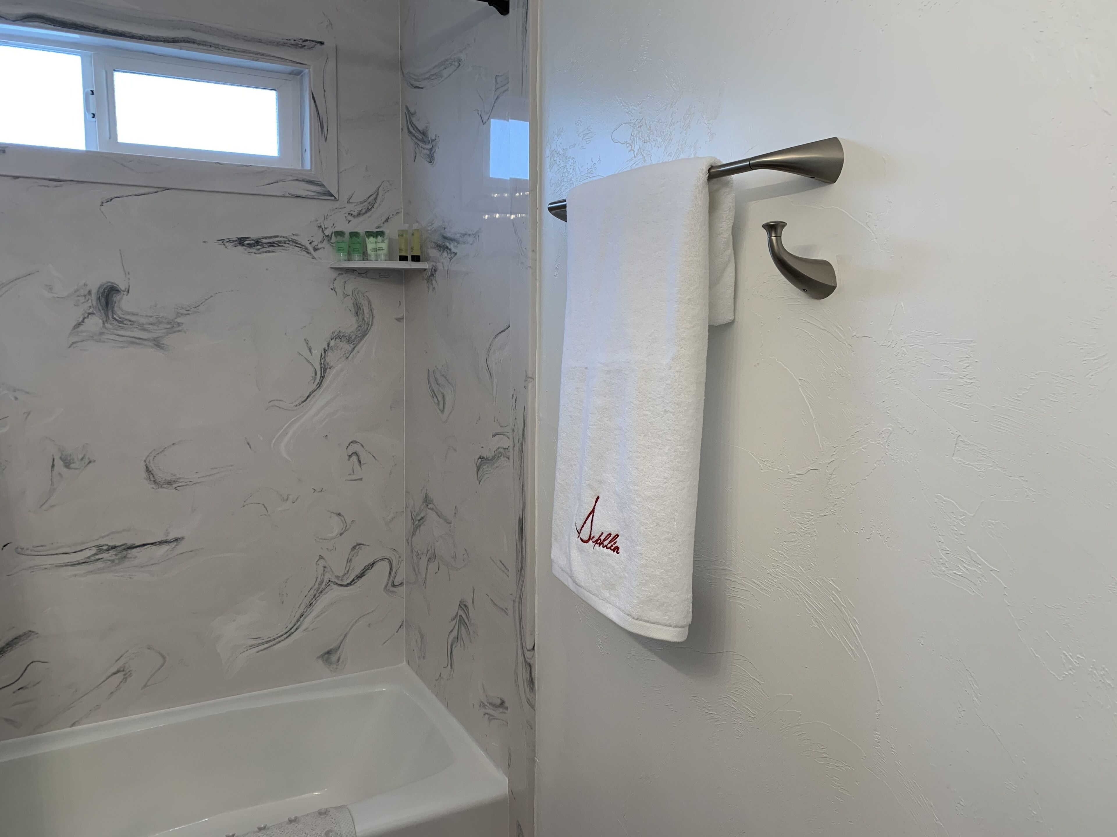 Une salle de bain avec une baignoire blanche, une serviette suspendue à un porte-serviettes fixé au mur, et une fenêtre située au-dessus de la baignoire.