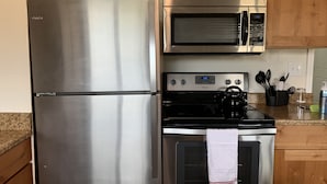 Un refrigerador de acero inoxidable, un microondas y un horno en una cocina con gabinetes de madera y encimeras de granito.