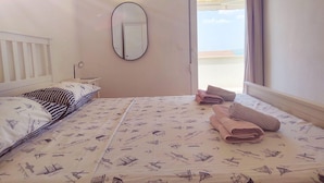 Een slaapkamer met een bed, nachtkastje, spiegel en een raam met uitzicht.