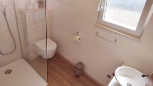 Een badkamer met een douchecabine van glas, een toilet, een bidet, een prullenbak en een wastafel.
