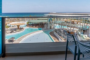 Vue d’ensemble de l’espace piscine d’un complexe hôtelier, avec plusieurs piscines, des zones de détente et un grand bâtiment en arrière-plan.