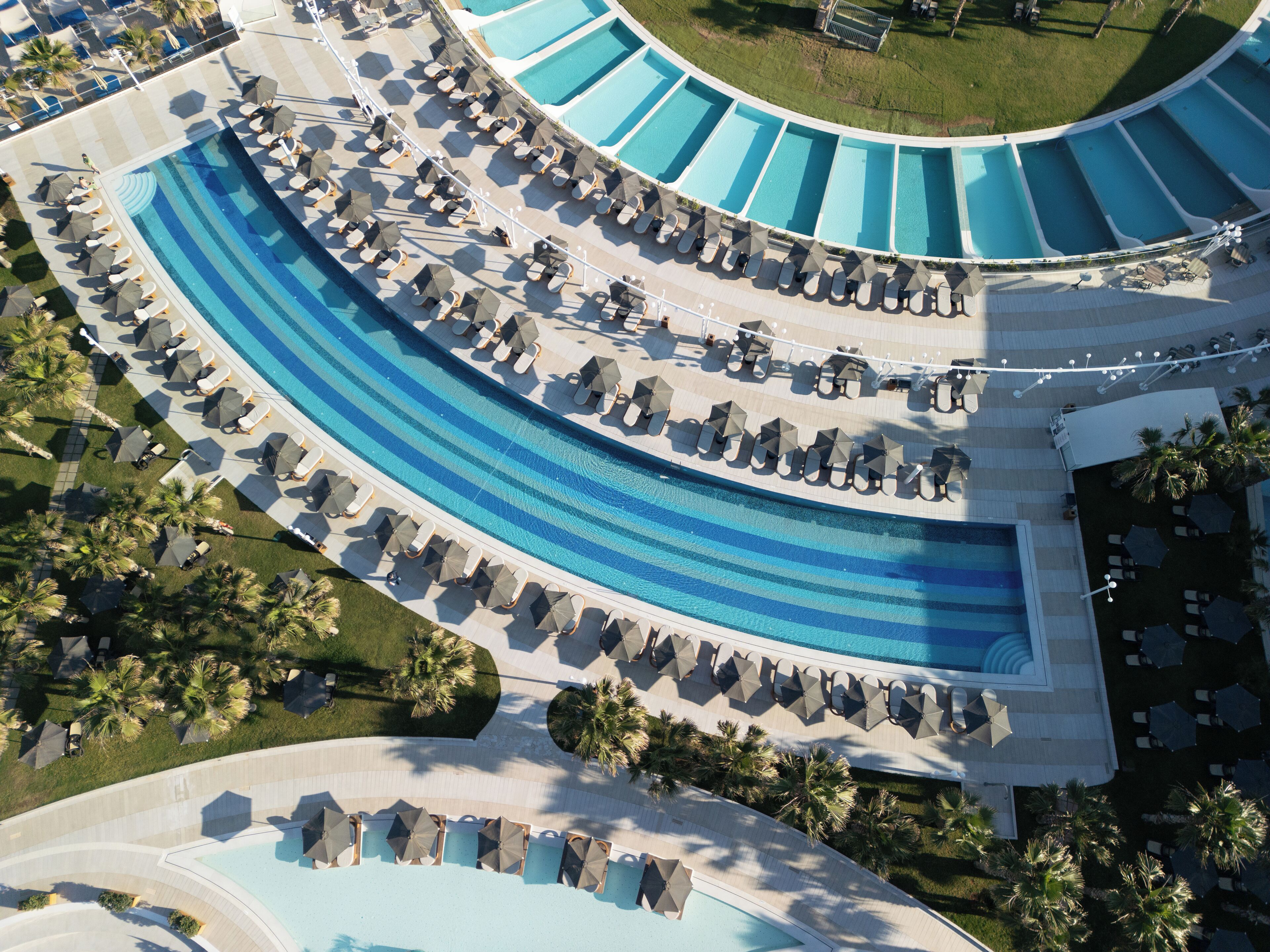 Una piscina grande y curvada con varias pistas, rodeada de sillas de descanso y sombrillas.