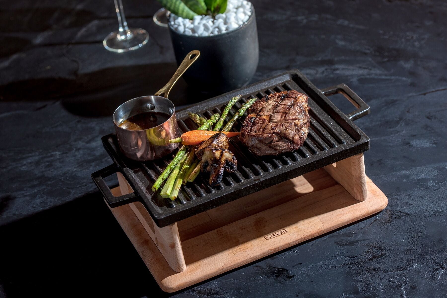 A portable grill with a steak and vegetables on a wooden stand.