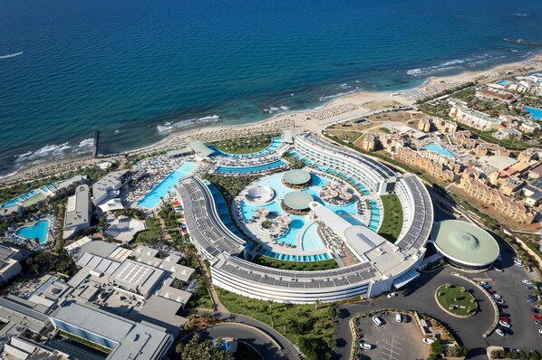 Vue aérienne d’un complexe hôtelier doté de plusieurs piscines, d’une plage et d’un parking.