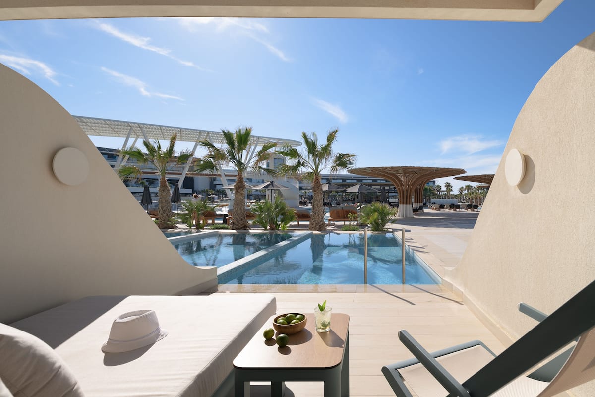 A poolside area with a view of a pool, palm trees, and a modern building in the background.