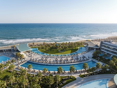 Een resort met een groot zwembad, palmbomen en uitzicht op het strand.