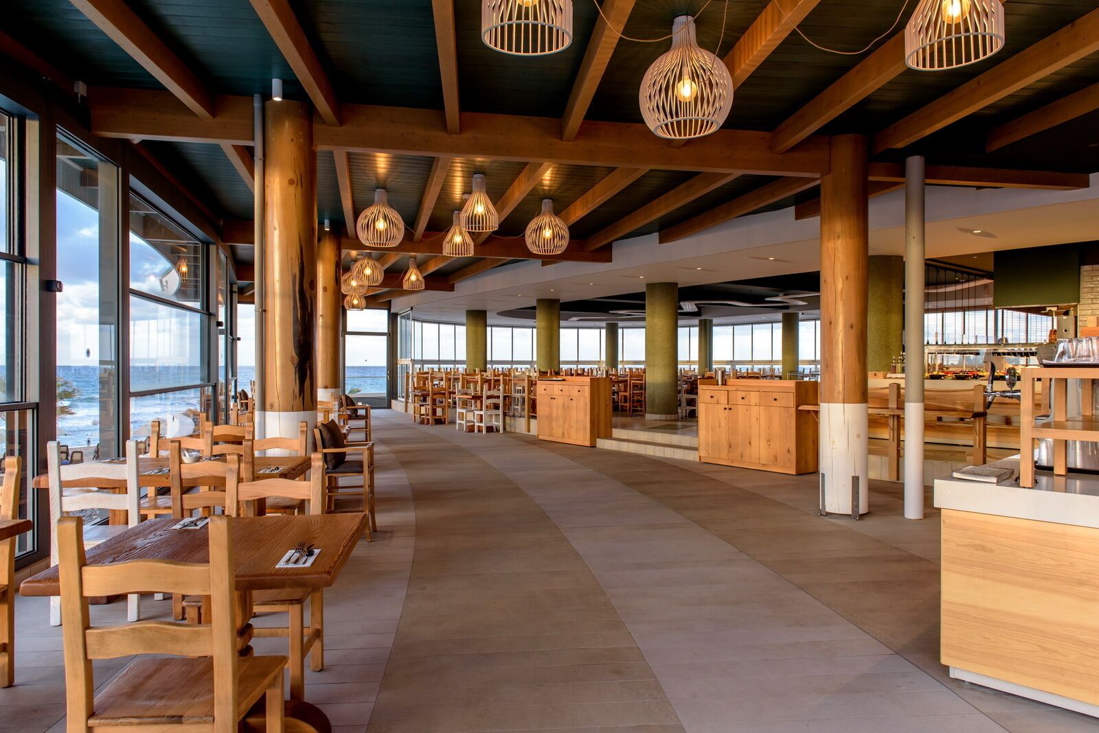 A spacious restaurant with wooden furniture, large windows, and hanging light fixtures.