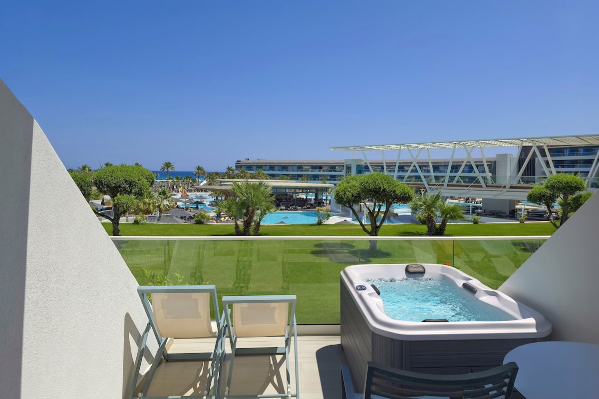 A balcony with a hot tub, chairs, and a view of a pool and resort buildings.