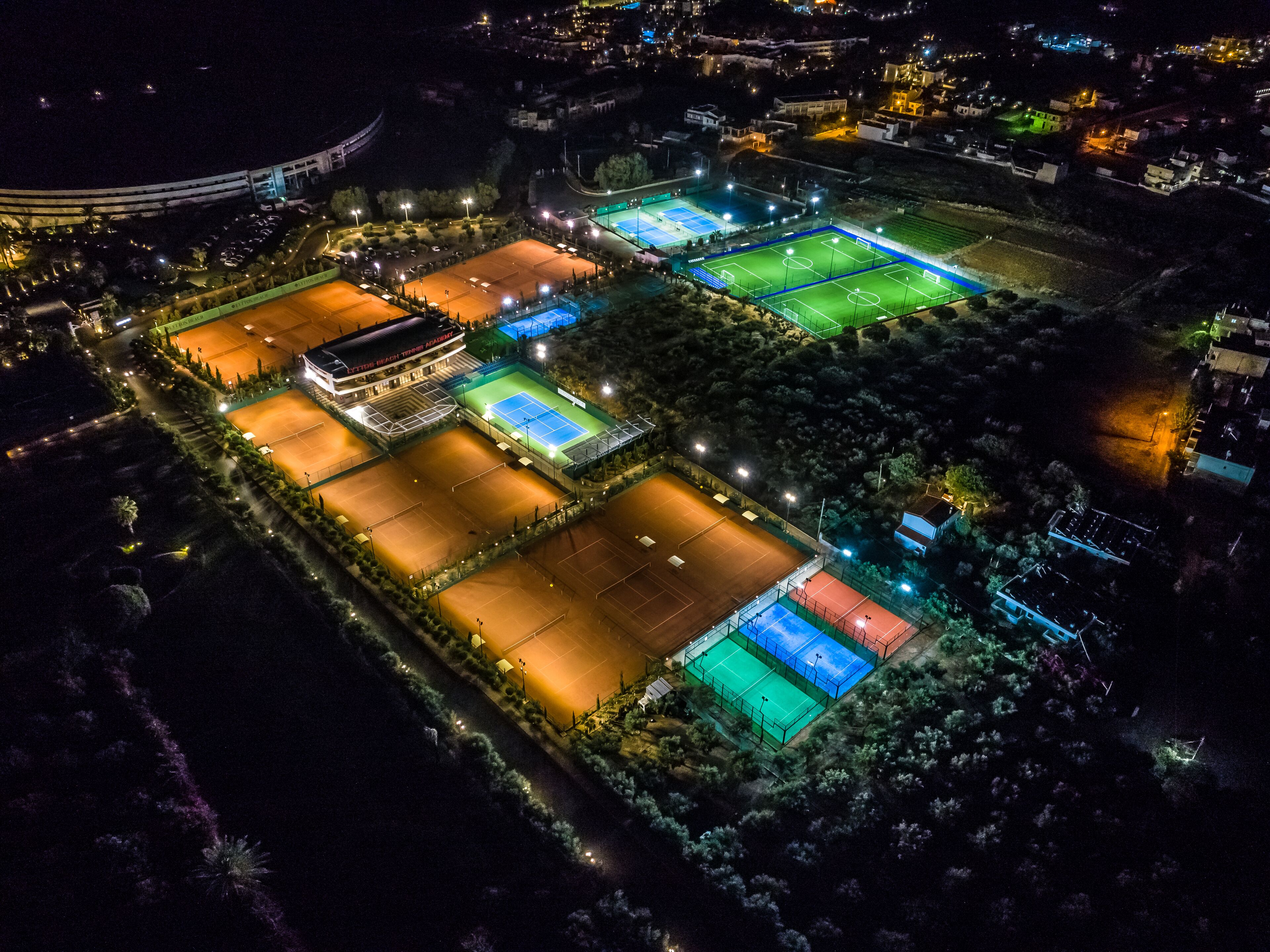 An aerial view of a sports complex with multiple tennis courts, a swimming pool, and a covered pavilion.