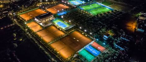 An aerial view of a sports complex with multiple tennis courts, a swimming pool, and a covered pavilion.