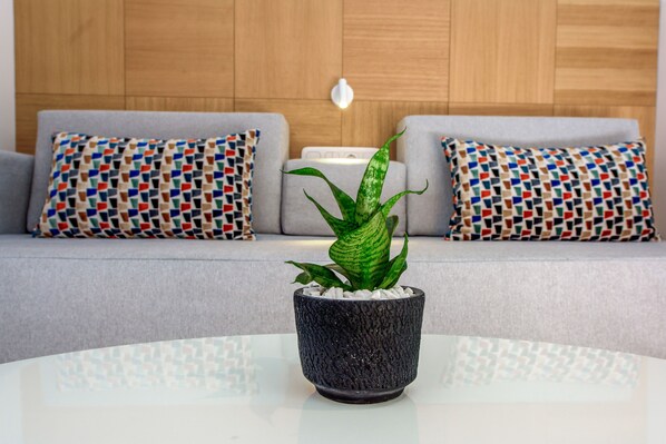 A modern living room with a grey sofa, patterned cushions, and a potted plant on a glass table. - Lyttos Mare Adults Friendly 12+ (Hersonissos)