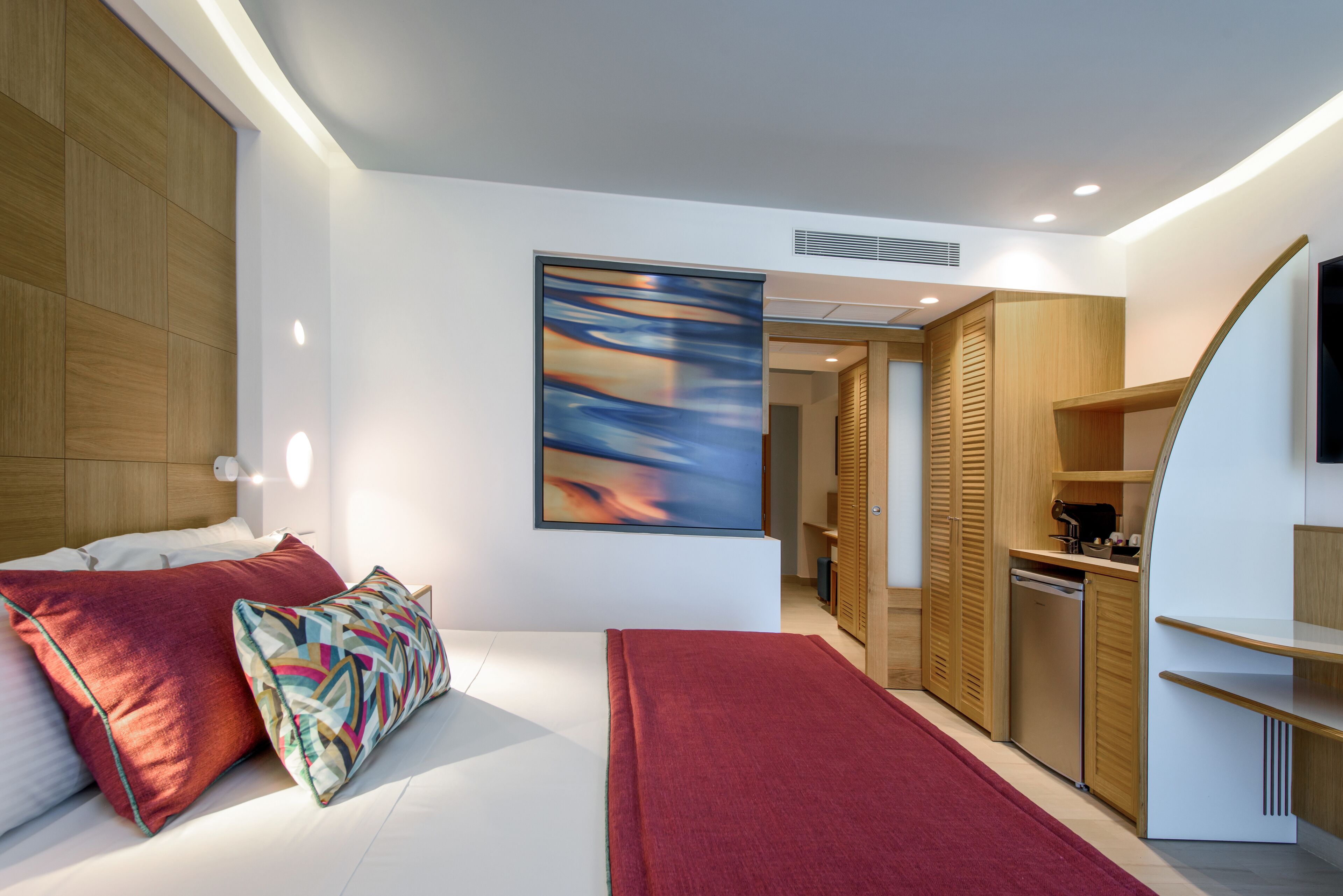 Un dormitorio moderno con cama, almohadas, una alfombra roja, un armario de madera y un cuadro en la pared.