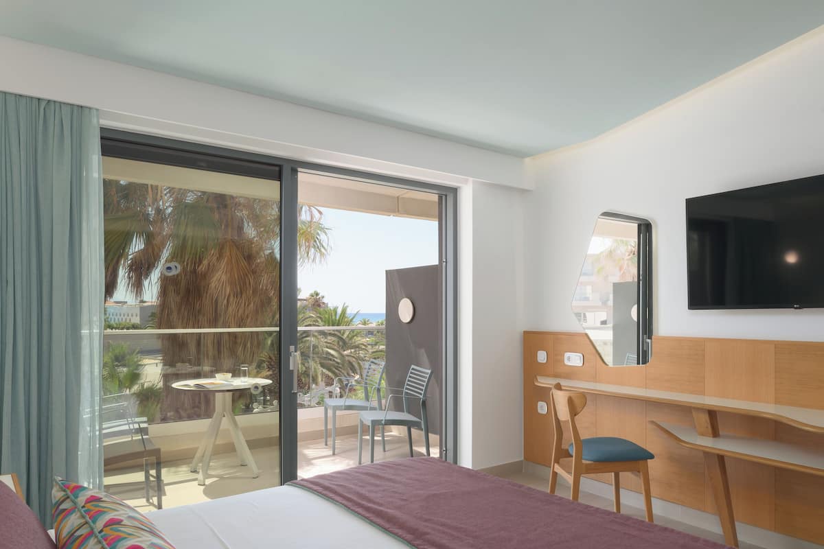 A hotel room with a bed, a desk, a chair, a TV, and a balcony with a table and chairs.