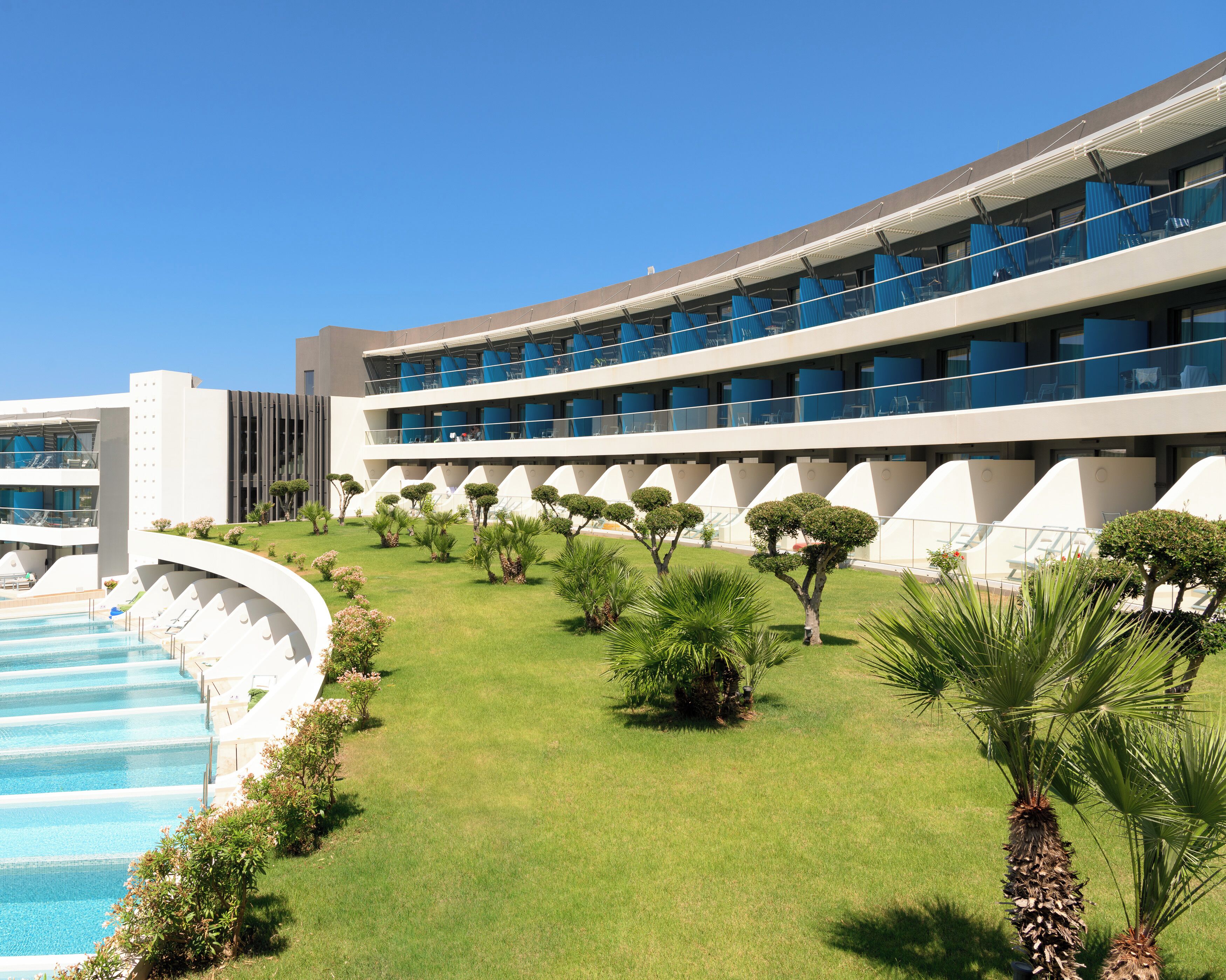 A modern hotel with a pool, multiple balconies, and well-maintained landscaping.