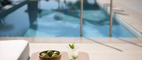A poolside setting with a wooden table holding a glass of drink and a bowl of limes.