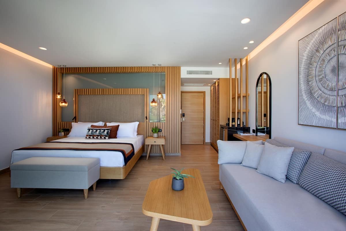 A modern hotel room with a bed, a sofa, a small table, and a mirror.