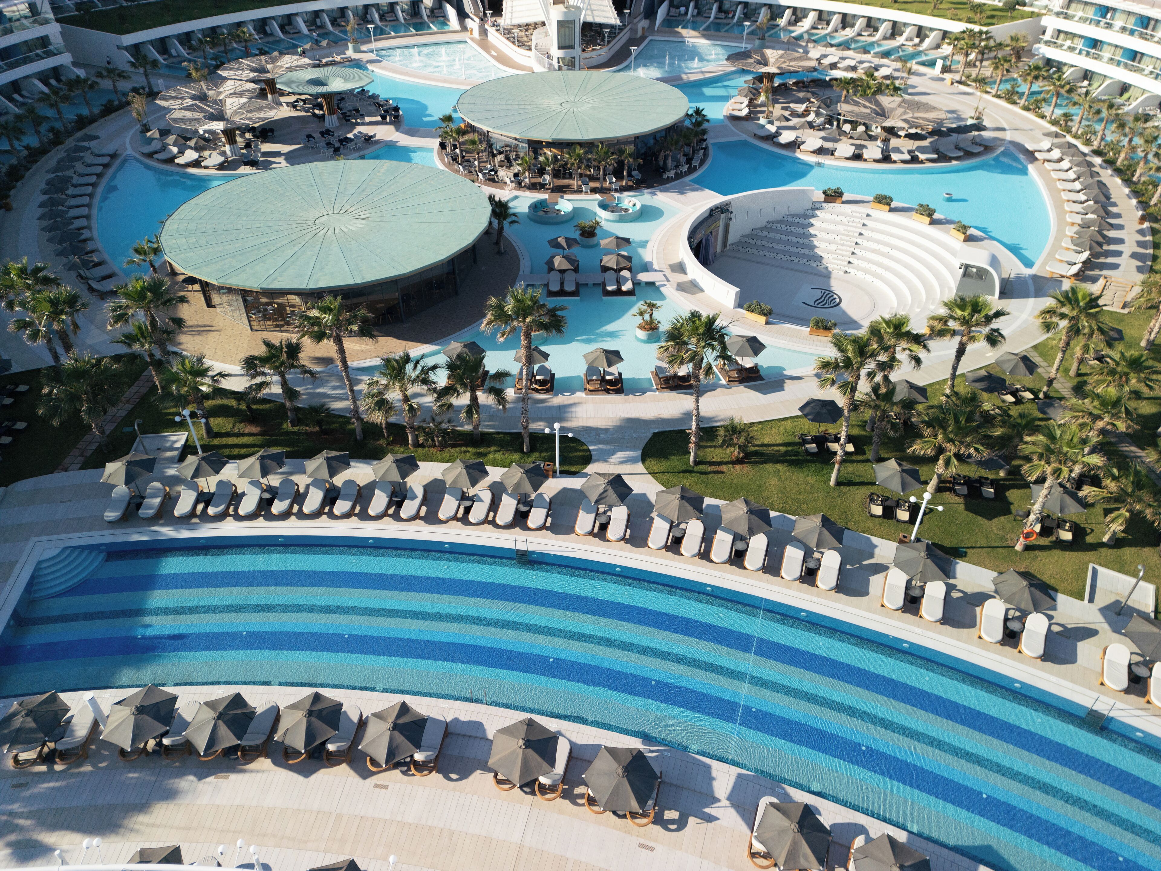 Una gran piscina de resort con varias secciones, palmeras y tumbonas.
