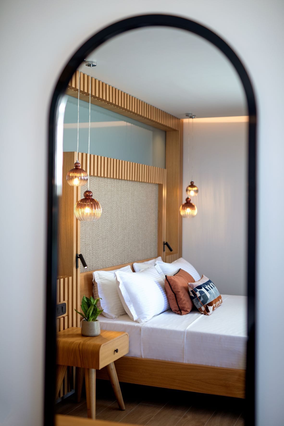 A modern bedroom with a wooden headboard, a bedside table with a lamp, and a bed with pillows and a blanket.