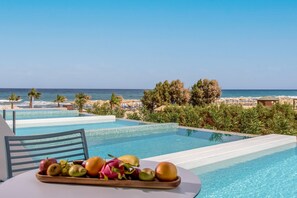 A poolside view with a table holding fruit, overlooking a beach with palm trees and a clear sky. - Lyttos Mare Adults Friendly 12+ (Hersonissos)