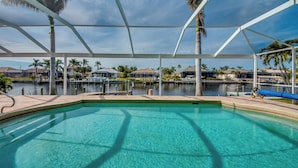 Ein Poolbereich mit klarem Wasser, einer überdachten Terrasse und Blick auf eine Marina mit Booten und Häusern im Hintergrund.
