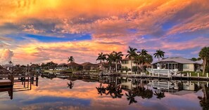 A marina with boats docked, a reflection of the sky in calm water, and palm trees. - Beautiful villa, extra large pool & west exposure in a tropical surrounding (Cape Coral)