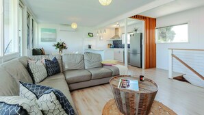 A modern living room with a sectional sofa, a round wicker coffee table, and a kitchen in the background. - Aldinga Beach Breakaway - Coastal Beauty Perfect For a Fam Vacay ~ C21 (Aldinga Beach)