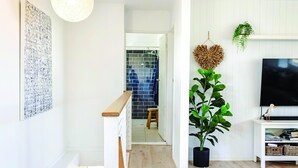 A modern living room with a staircase, a large potted plant, a flat-screen TV, and a wall-mounted shelf. - Aldinga Beach Breakaway - Coastal Beauty Perfect For a Fam Vacay ~ C21 (Aldinga Beach)