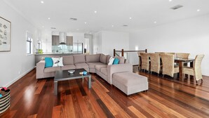 A modern living room with a sectional sofa, a dining table with wicker chairs, and hardwood flooring. - Percival Point ~ Port Willunga - Sweeping Pt. Willunga Sea Views (Port Willunga)