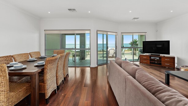 A modern living room with a dining area, large windows, a TV, and a view of the ocean. - Percival Point ~ Port Willunga - Sweeping Pt. Willunga Sea Views (Port Willunga)