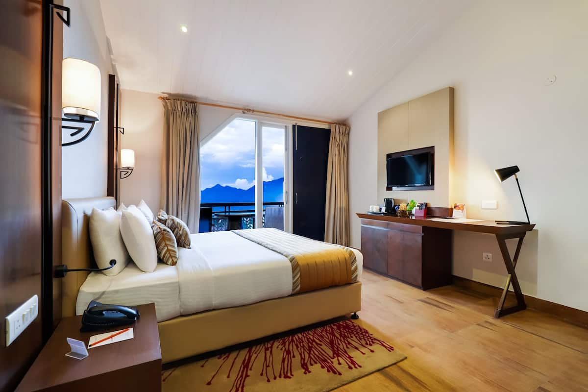 A hotel room with a bed, desk, TV, and a view of mountains.