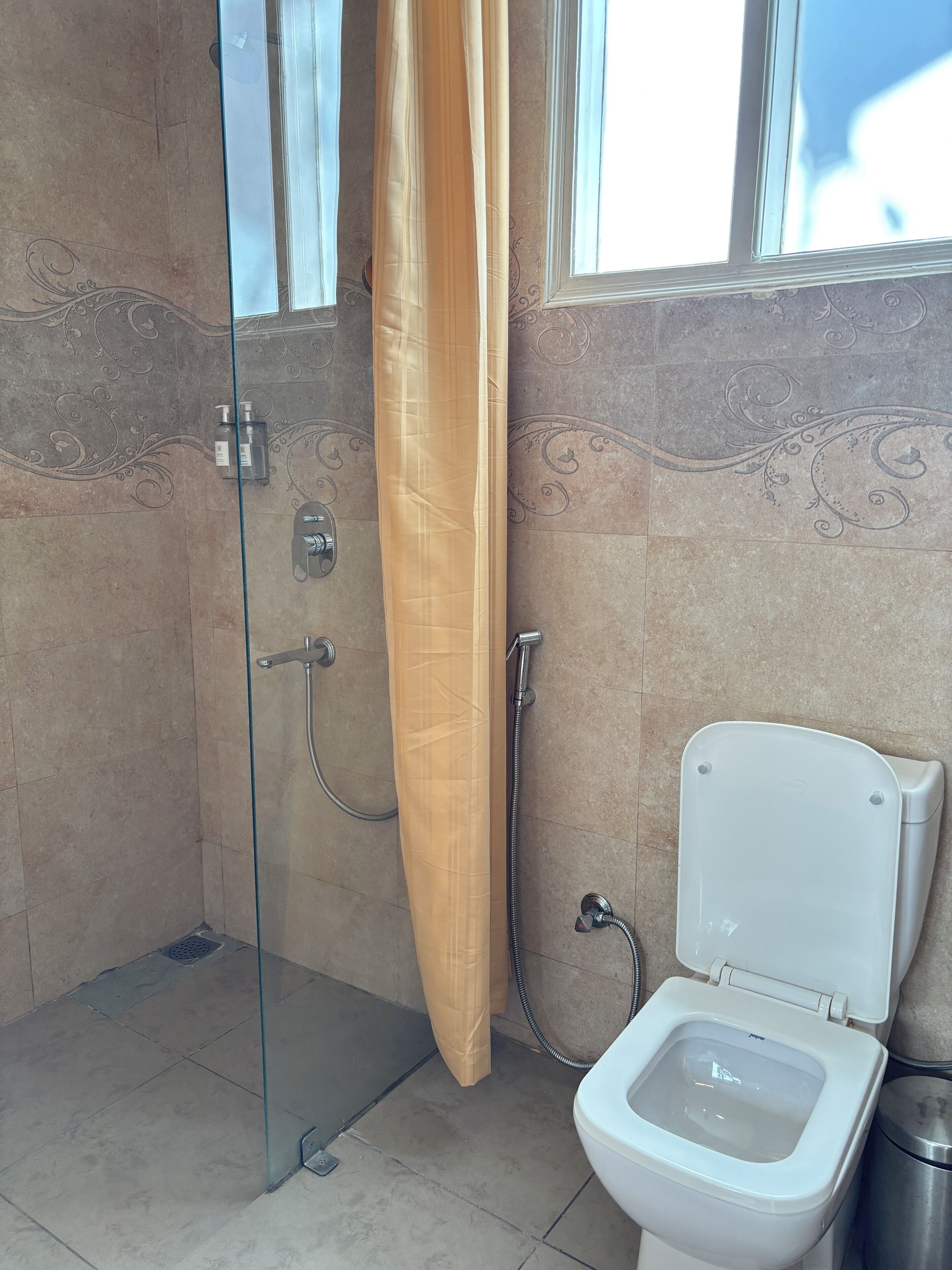 A bathroom with a glass shower enclosure, a toilet, and a window.