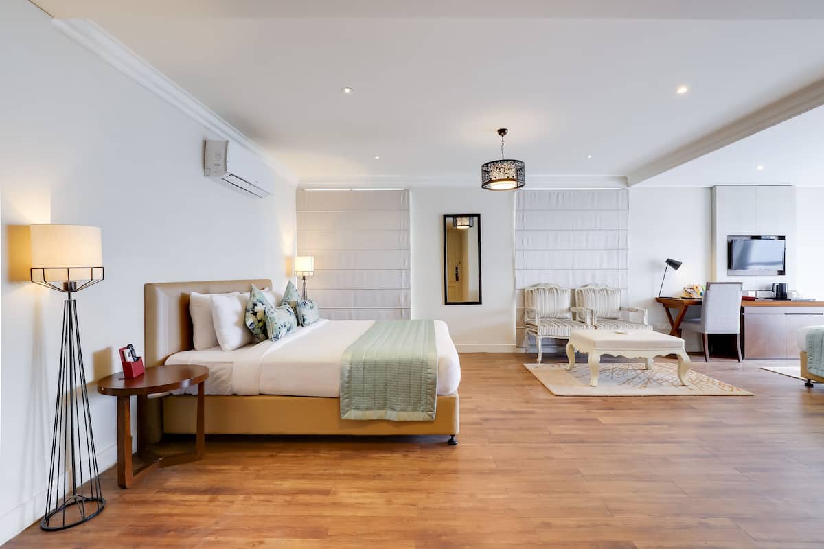 A modern hotel room with a bed, bedside table, lamp, and a desk with a chair.