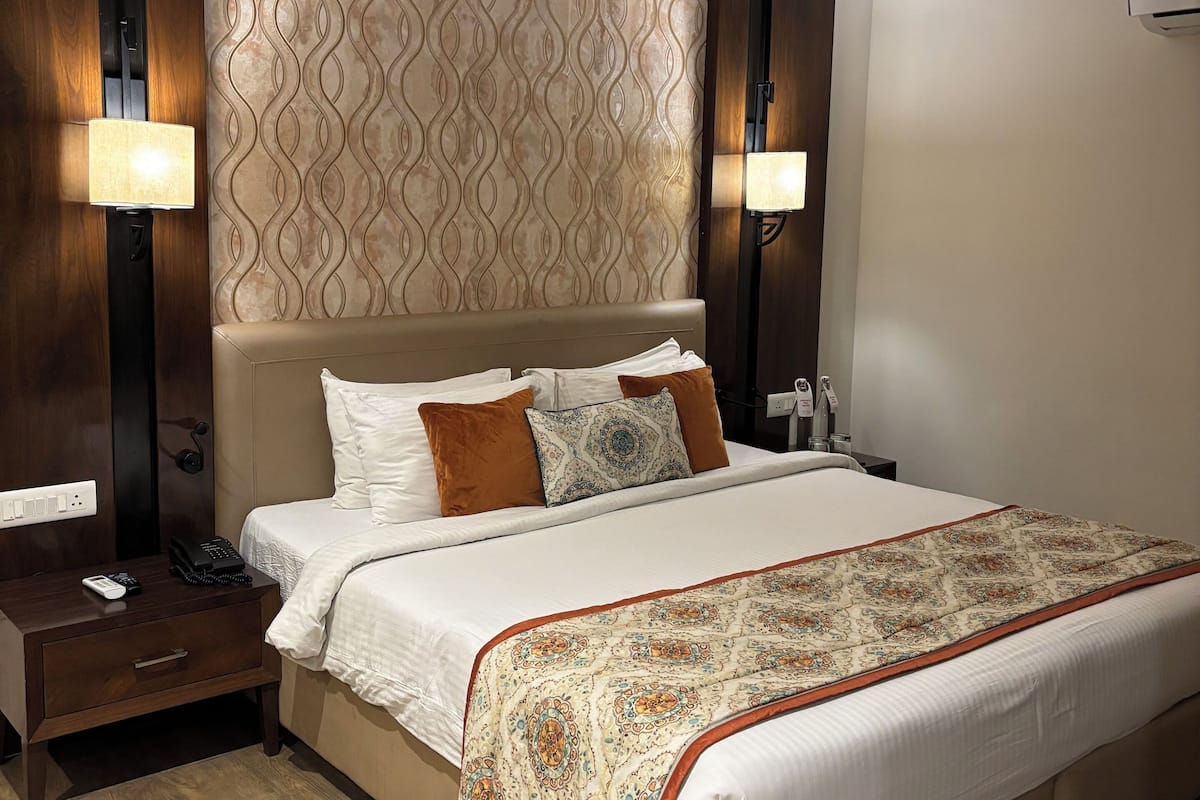 A hotel room with a large bed, two bedside tables, a nightstand, a patterned wall, and two wall-mounted lamps.